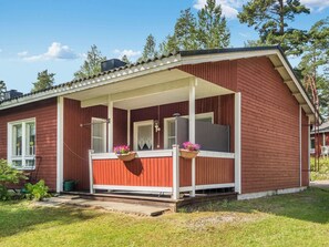 A red wooden house with a porch, two flower baskets, and a clear sky.