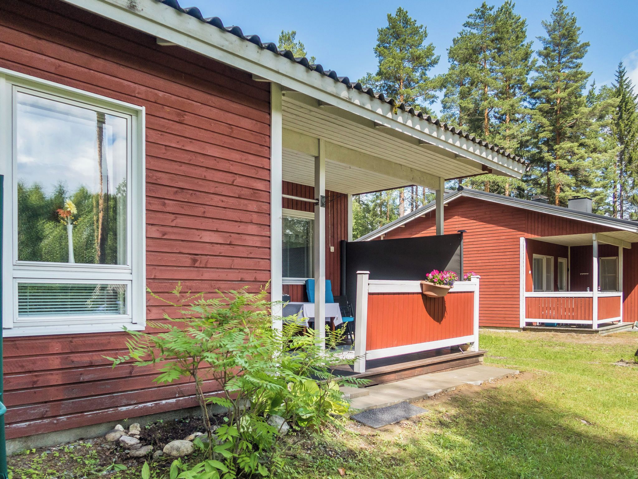 Ein rotes Holzhaus mit überdachter Veranda, einem Fenster mit Blume und einem kleinen Garten.