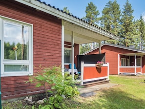 A red wooden house with a covered porch, a window with a flower, and a small garden area. - Lomakatti 6b by Interhome (Sotkamo)