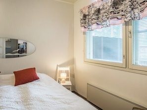 Habitación de hotel con cama, mesita de noche, lámpara, ventana con persianas y espejo adosado a la pared.