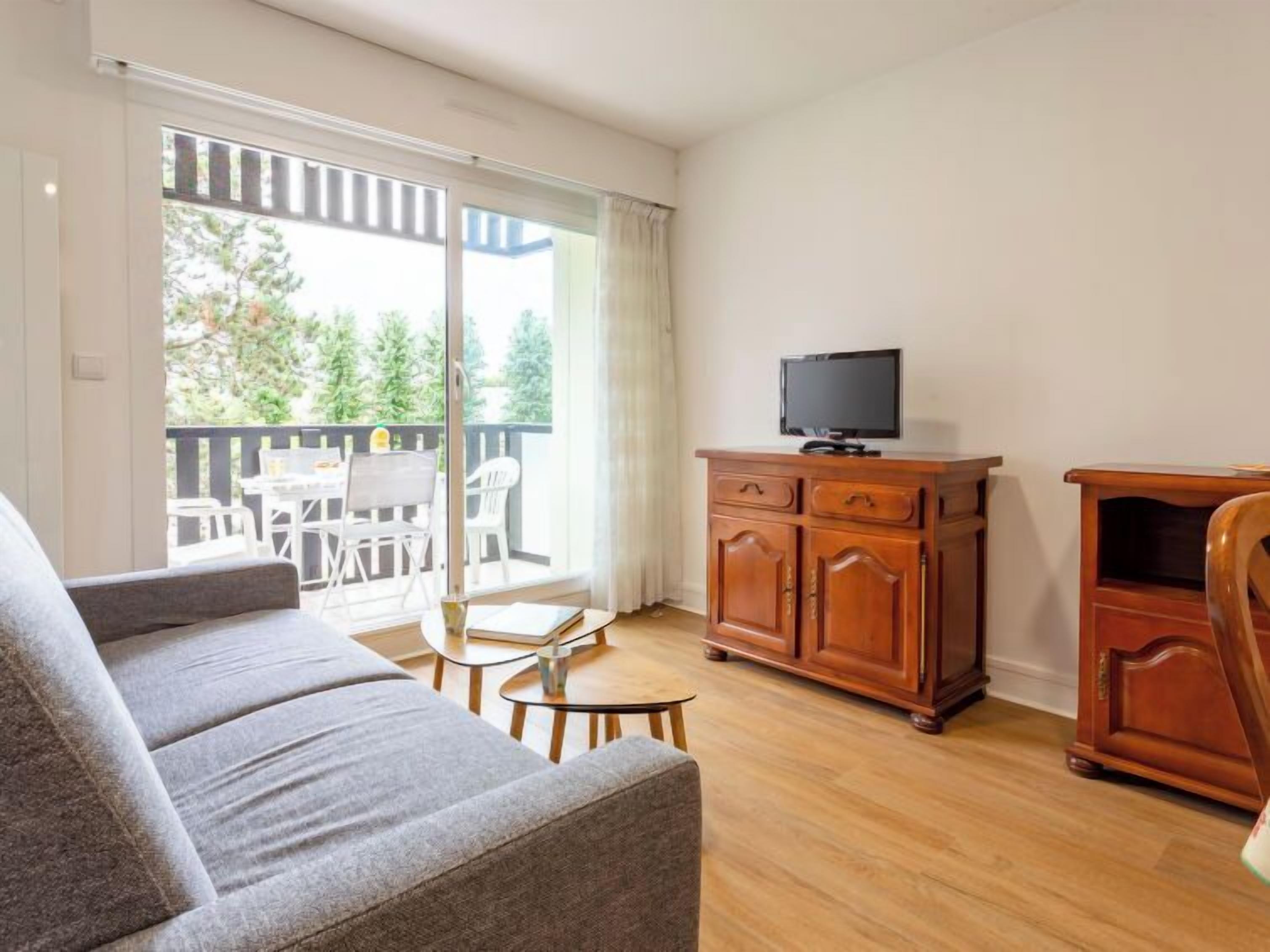 A living room with a sofa, a TV on a wooden cabinet, and a balcony with outdoor furniture.