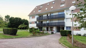 Ein mehrstöckiges Wohnhaus mit einem zentralen Eingang, Balkonen und einem gepflegten Garten.