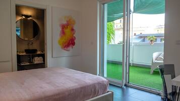 A bedroom with a bed, a bathroom with a mirror, a window, and a balcony with a chair.