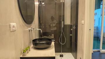 Een moderne badkamer met een grote spiegel, een zwarte wastafel en een douche met glazen wanden.
