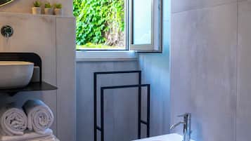 A modern bathroom with a large window, a round sink, a bidet, and a toilet.