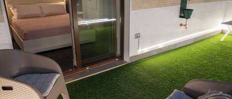 A modern outdoor seating area with wicker furniture and a glass door leading to a bedroom.
