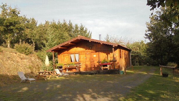 Une cabane en bois avec une véranda, une table de pique-nique et deux chaises longues.