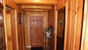 Un couloir en bois avec une porte, un présentoir métallique avec un panier, et un luminaire fixé au mur.