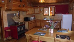 Une cuisine chaleureuse avec des meubles de rangement en bois, un réfrigérateur rouge, un four à micro-ondes et une table à manger avec des chaises.