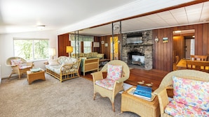 A spacious living room with wicker furniture, a stone fireplace, and large windows. - Baboosic Lake - Wonderful Classic S. NH Vacation Cottage all to Yourself (Merrimack)