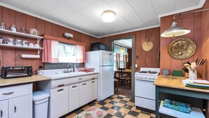 A compact kitchen with white cabinets, a microwave, a refrigerator, a sink, and a stove. There is a checkered floor, a small rug, and a hanging light fixture. - Baboosic Lake - Wonderful Classic S. NH Vacation Cottage all to Yourself (Merrimack)