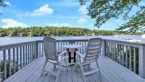 A deck with two white chairs and a small table, overlooking a lake with a view of a forested area and a distant shoreline. - Baboosic Lake - Wonderful Classic S. NH Vacation Cottage all to Yourself (Merrimack)