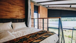 A bedroom with a large bed, a view of a lake, and a balcony with a railing. - UMVA Muhazi (Muhazi)