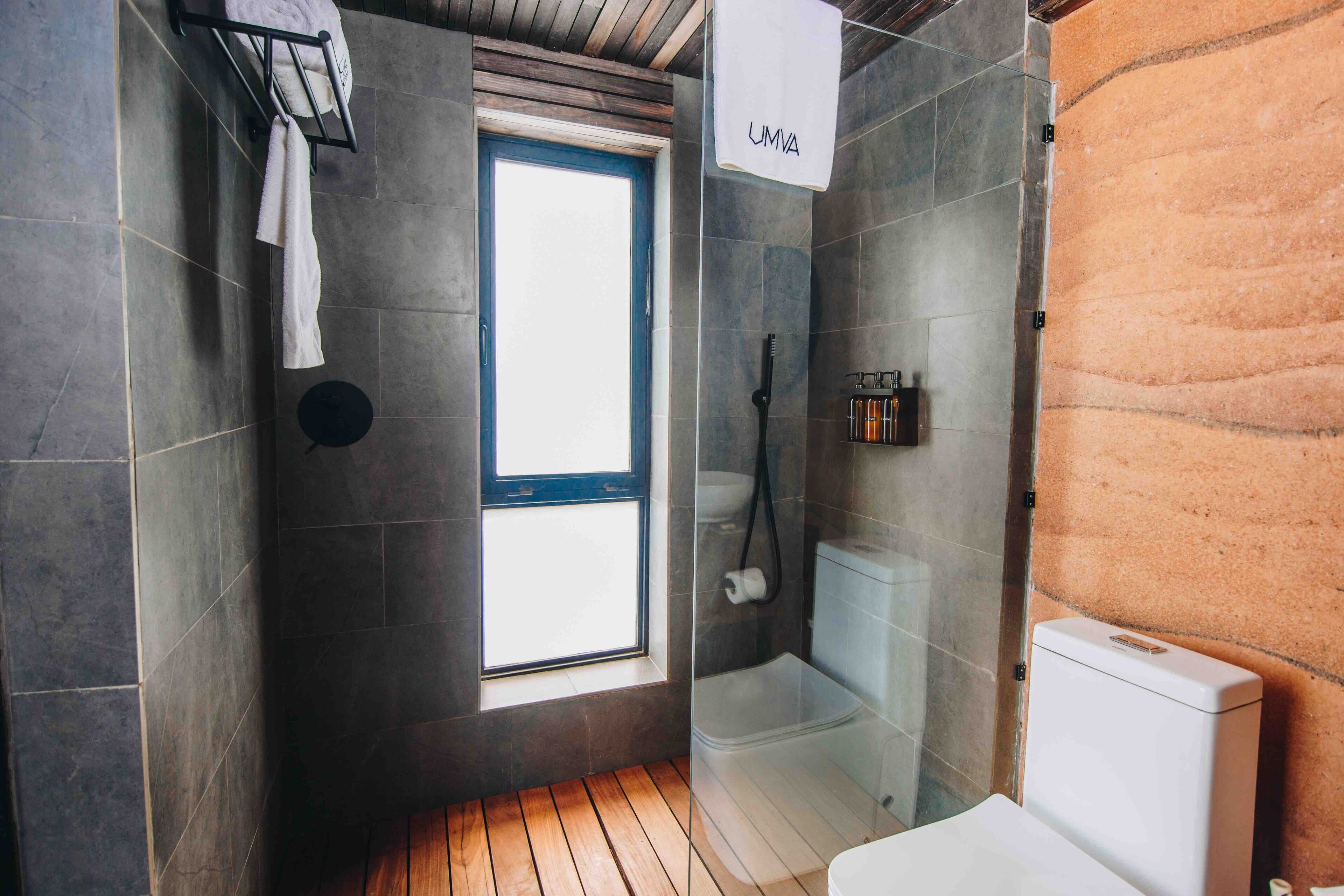 A bathroom with a window, a towel rack, a toilet, and a shower area.