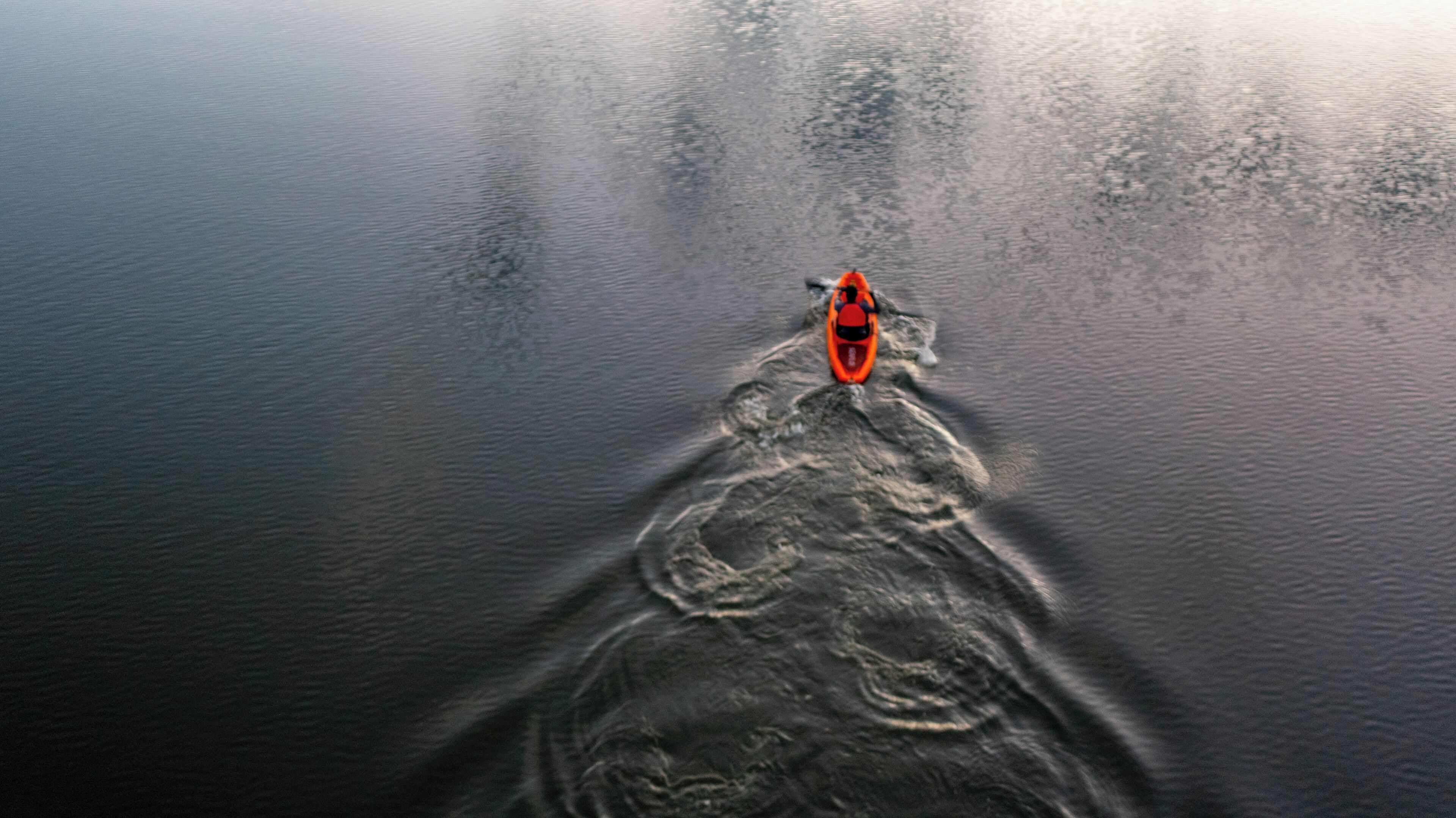A kayak on a calm body of water with a wake behind it.