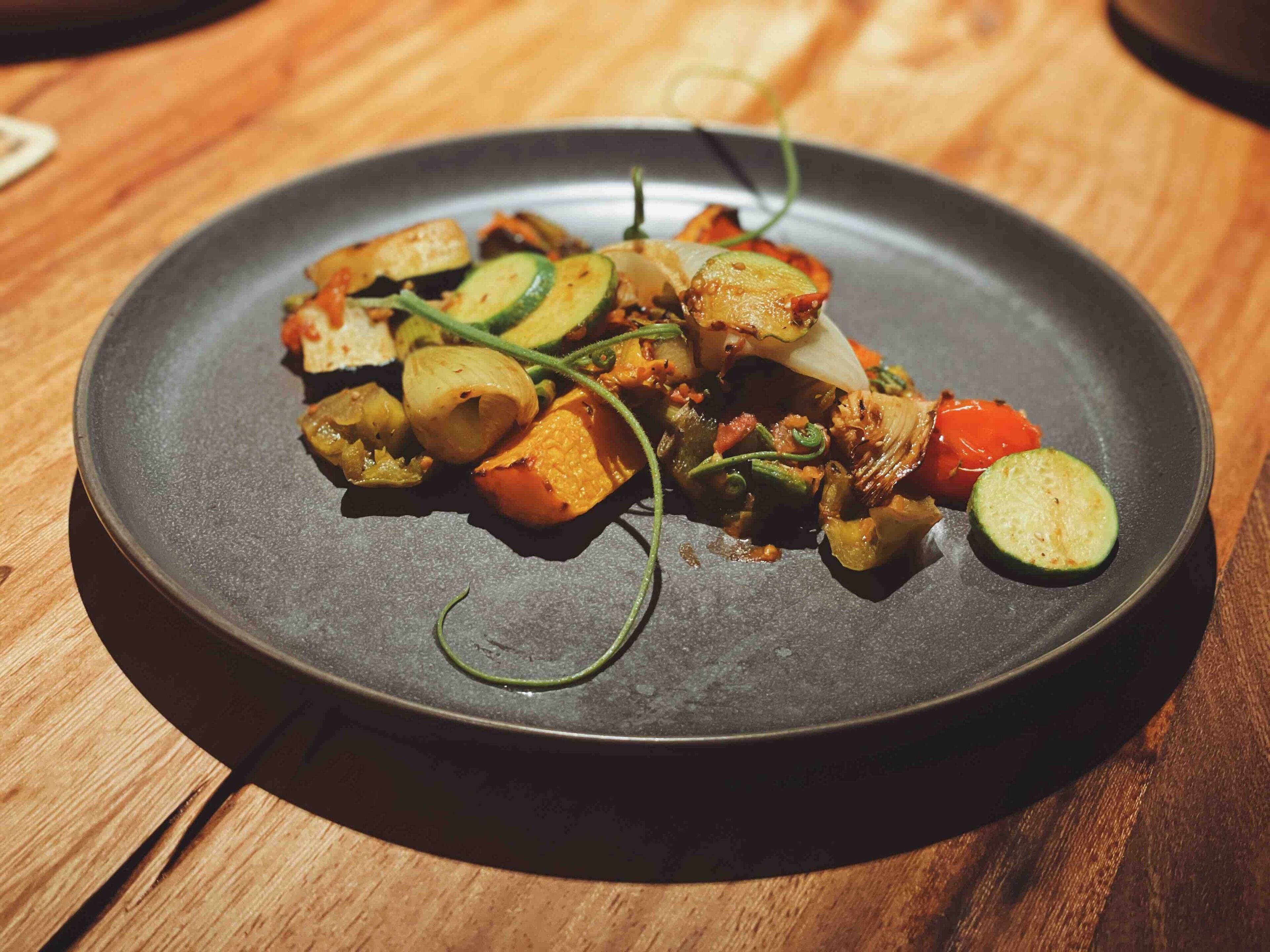 A plate of roasted vegetables on a dark plate.