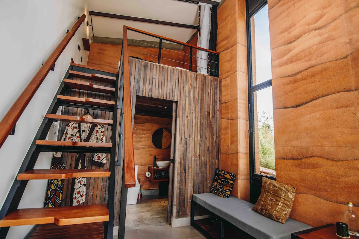 A staircase with wooden steps and a metal railing, leading to a loft area with a wooden wall and a window.