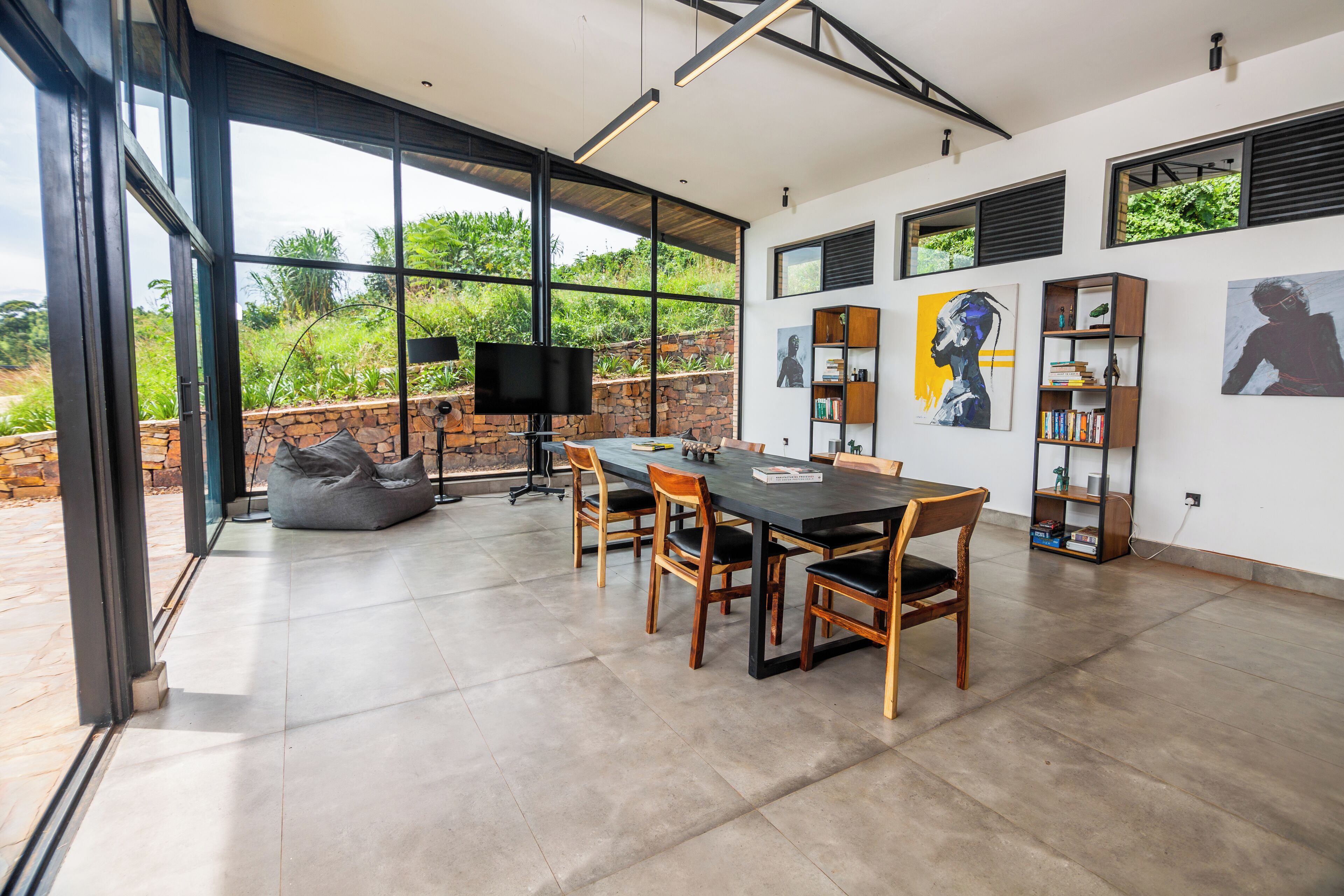 A modern dining area with a large table, chairs, and a television. There are bookshelves and artwork on the walls.