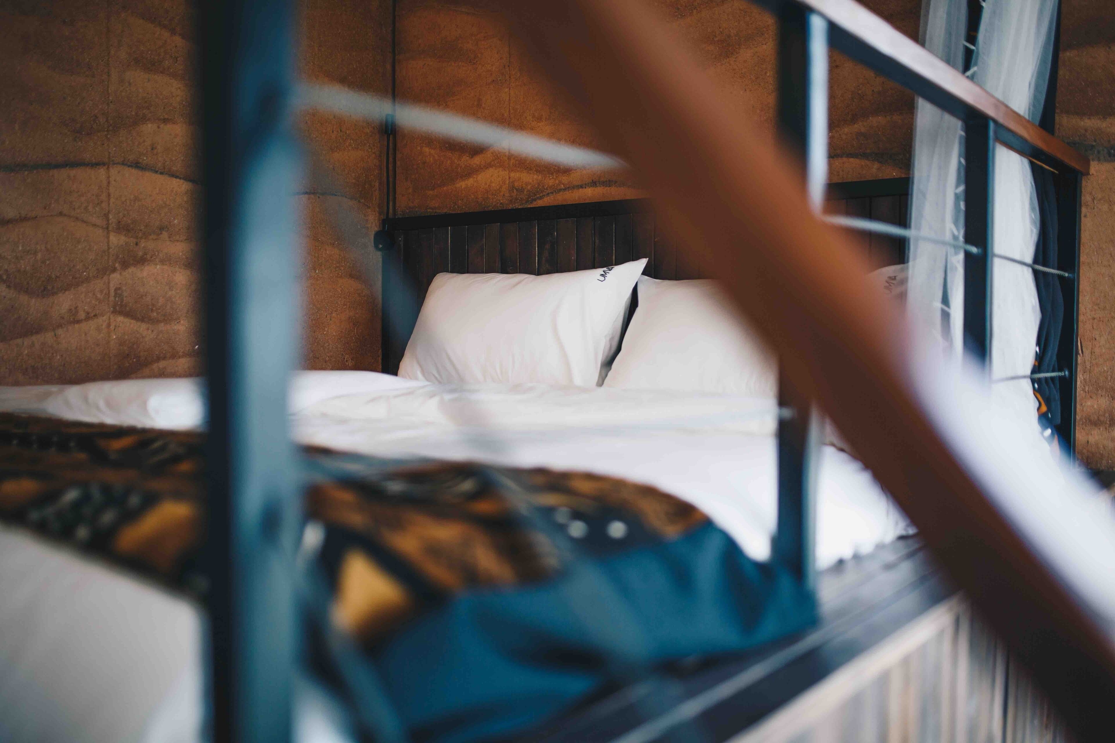 A bed with white bedding and a headboard, a wooden frame, and a window with curtains.