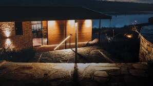 A stone staircase leading to a wooden door with a glass panel, surrounded by a stone wall and a view of a lake at dusk. - UMVA Muhazi (Muhazi)
