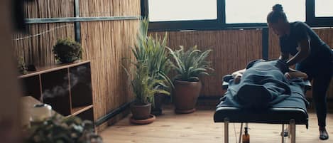 Una habitación con una mesa de masajes, plantas en macetas y una pared de bambú.