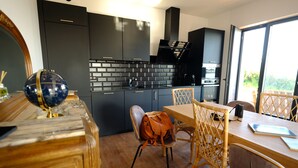 Eine moderne Küche mit dunklen Schränken, einer Zierleiste aus Ziegelsteinen und einem Essbereich mit Holztisch und Korbstühlen.