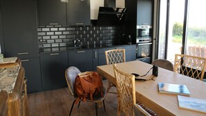 Eine moderne Küche mit dunklen Schränken, einer Ziegelrückwand und einem Essbereich mit Holztisch und Stühlen.