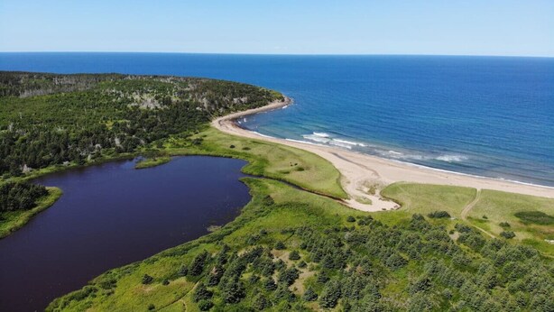 Vue aérienne d’une zone côtière comprenant un lac, une plage et une zone boisée.