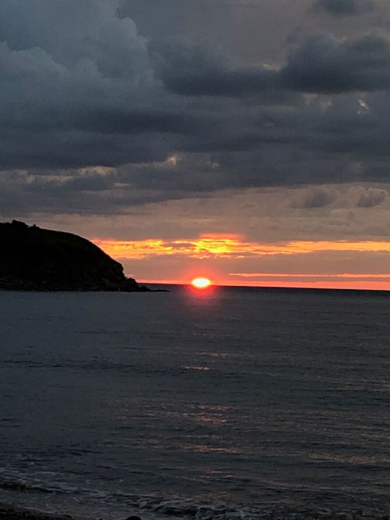 Un atardecer sobre un mar tranquilo con un litoral rocoso.