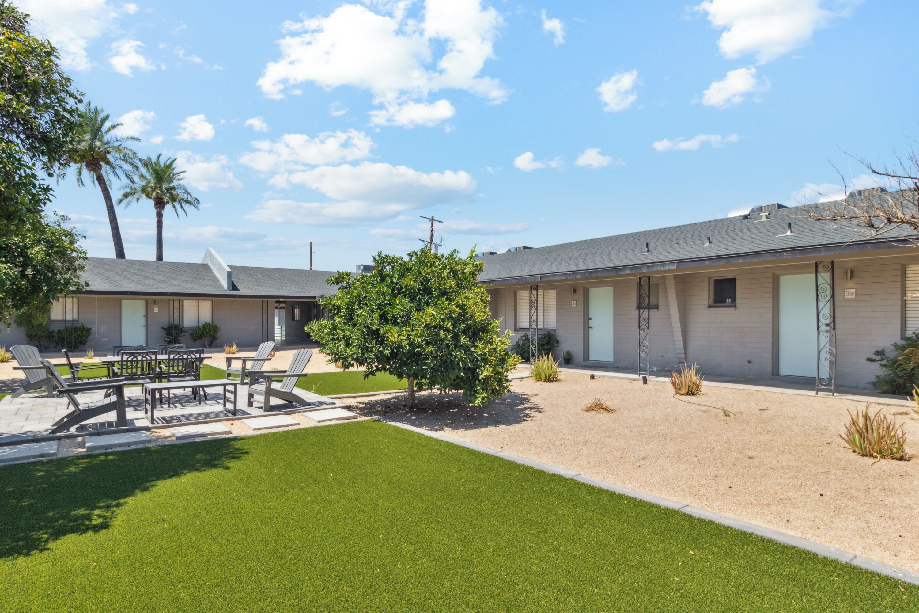 A modern motel with a well-maintained lawn, outdoor seating area, and a clear view of the sky.