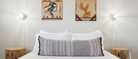 A bed with white and gray bedding, two wooden nightstands, and two wall-mounted lights.