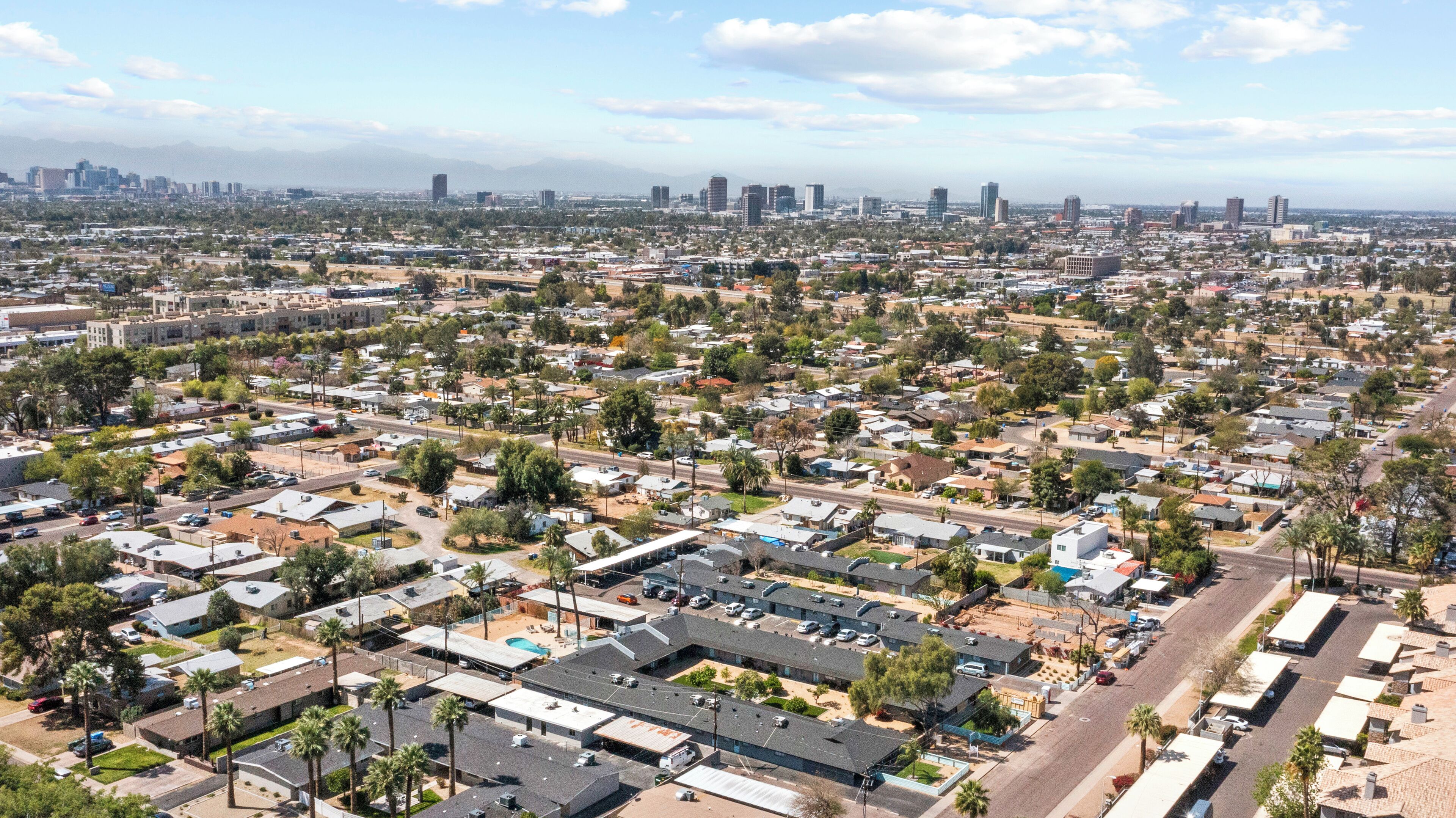 Vista aérea de una zona residencial con casas unifamiliares y edificios de apartamentos, rodeada de vegetación y un horizonte urbano lejano.