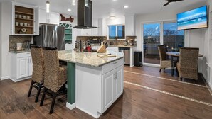 A modern kitchen with white cabinets, a large island, and a dining area with wicker chairs.