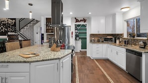 A modern kitchen with white cabinets, a large island, stainless steel appliances, and a patterned backsplash.