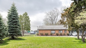 A single-story brick building with a flat roof, surrounded by a well-maintained lawn and several evergreen trees. - 2Bd Holiday Retreat Detroit Museums and Parks (Riverview)