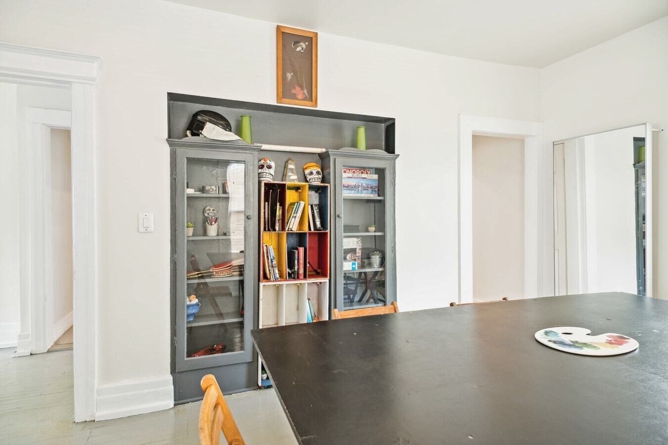 A room with a large black table, a bookshelf with various items, and a framed picture on the wall.