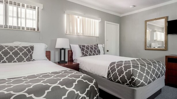 A hotel room with two beds, a nightstand, a lamp, a mirror, and a door. - Browntown Room for 4: Comfort, Wifi & Parking (Riverview)
