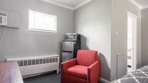 A bedroom with a red armchair, a white radiator, a small refrigerator, and a bed with a patterned bedspread. - Browntown Room for 4: Comfort, Wifi & Parking (Riverview)