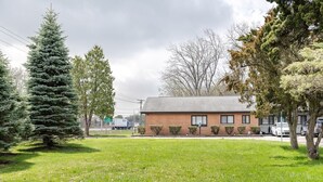 A single-story brick building with a flat roof, surrounded by a well-maintained lawn and several evergreen trees. - Browntown Room for 4: Comfort, Wifi & Parking (Riverview)