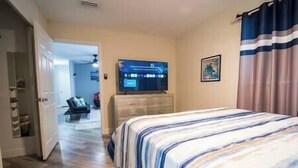 A hotel room with a bed, a television, a dresser, and a door leading to another room. - Bacolet Beach Cottage-Luxe Pool (Palm Beach Gardens)