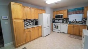 A kitchen with wooden cabinets, a refrigerator, a microwave, an oven, and a sink. - Bacolet Beach Cottage-Luxe Pool (Palm Beach Gardens)