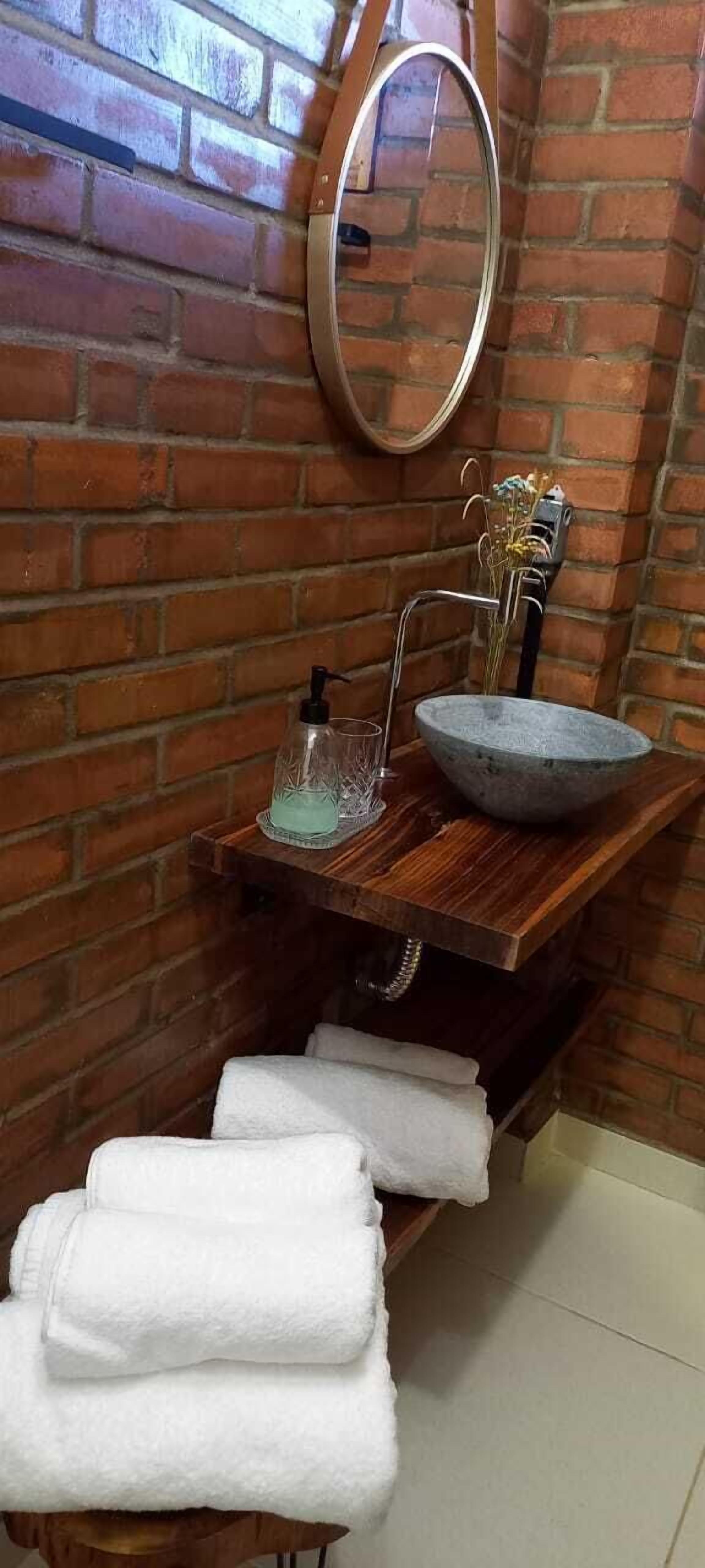 Un baño con tocador de madera, un espejo redondo, un lavabo de piedra y un perchero con toallas dobladas.