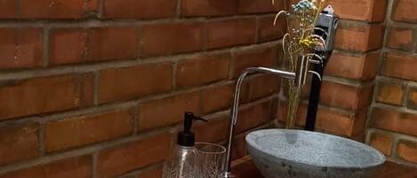 Un baño con tocador de madera, un espejo redondo, un lavabo de piedra y un perchero con toallas dobladas.