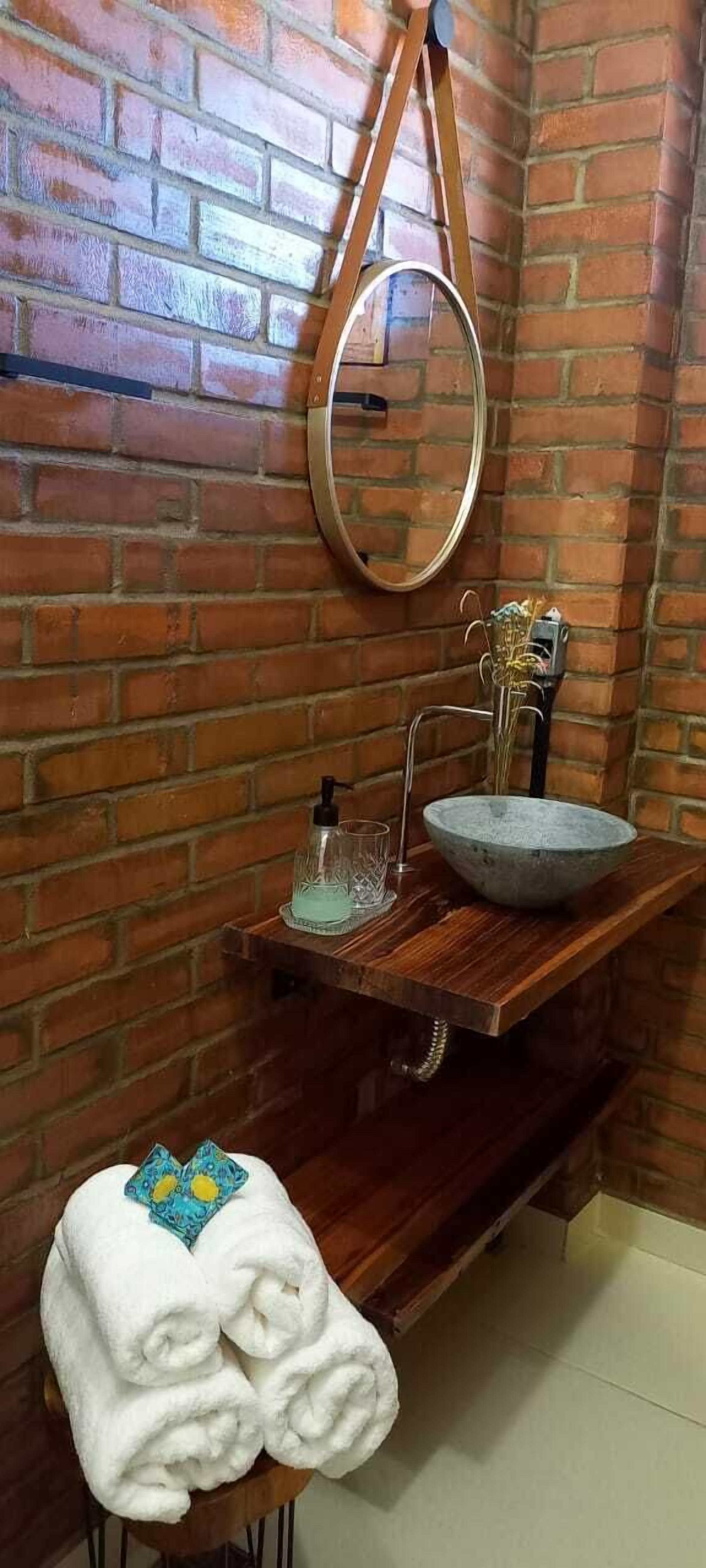 A bathroom with a wooden vanity, a round mirror, a stone sink, and a towel rack with a folded towel.
