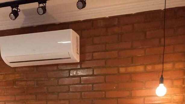 A room with a brick wall, a bed with white bedding, a hanging light bulb, and a small wooden stool. - Pousada Bem Viver (Nobres)
