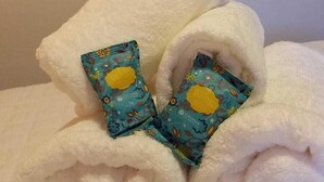 A neatly folded white towel with a colorful pillow on a bed. - Pousada Bem Viver (Nobres)