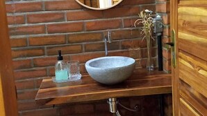 A bathroom with a wooden vanity, a round mirror, a vessel sink, and a hanging towel rack. - Pousada Bem Viver (Nobres)