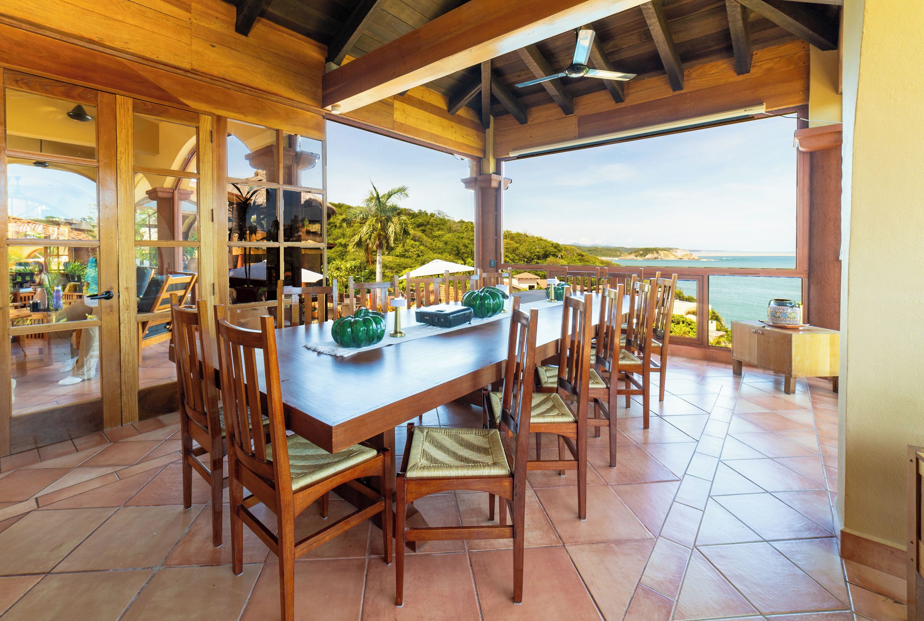 Un comedor techado con una mesa larga y sillas, con vistas a un paisaje marino.