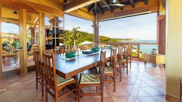 Un comedor techado con una mesa larga y sillas, con vistas a un paisaje marino.