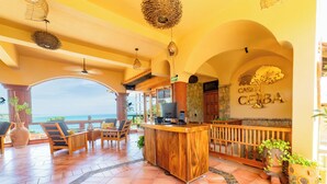 A spacious indoor area with a wooden reception desk, seating arrangements, and a view of the ocean. - Casa Ceiba Huatulco - Adults Only (Santa María Huatulco)